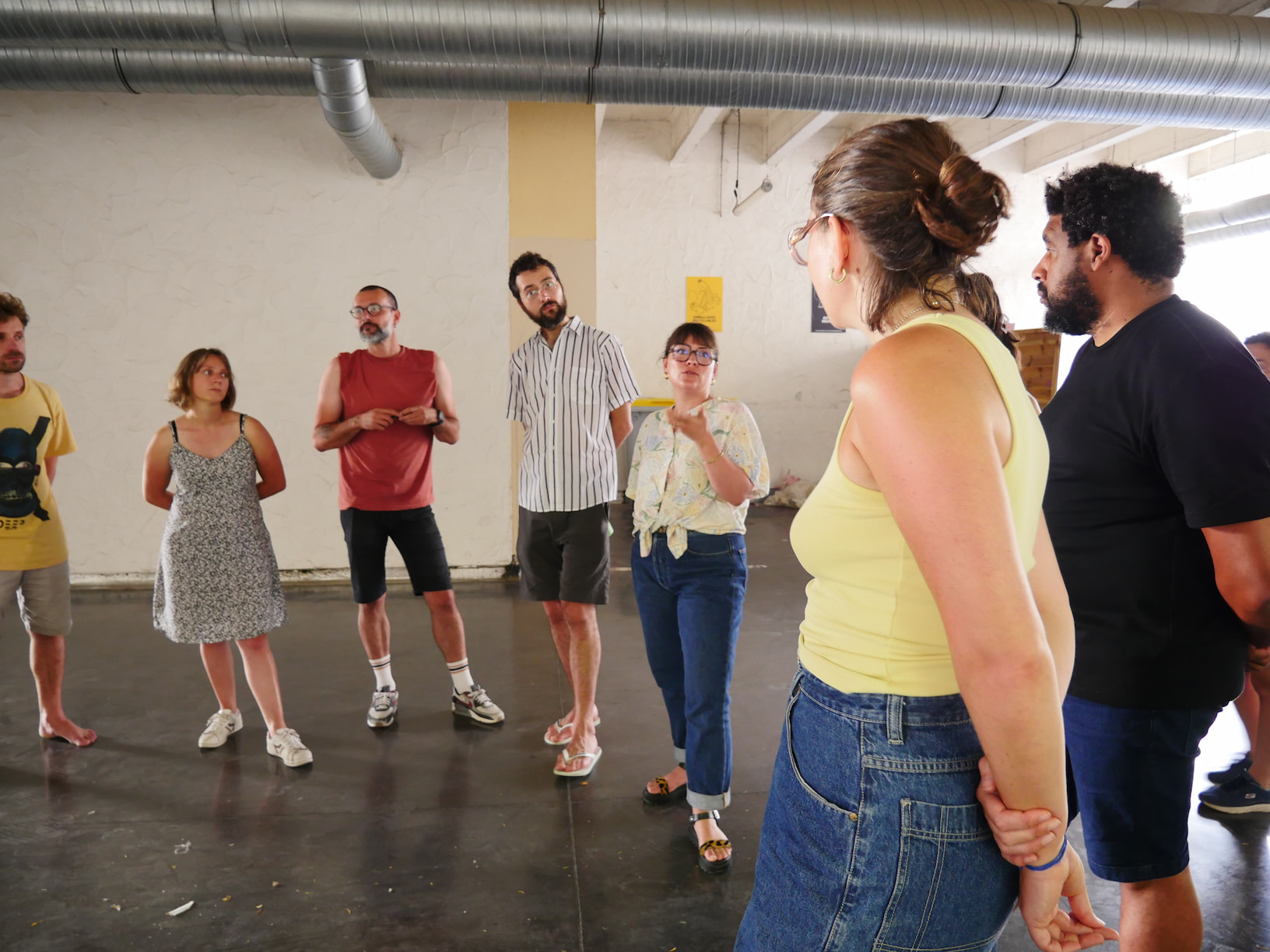 Groupe de personnes en cercle dans un espace intérieur, écoutant une femme parler au centre.