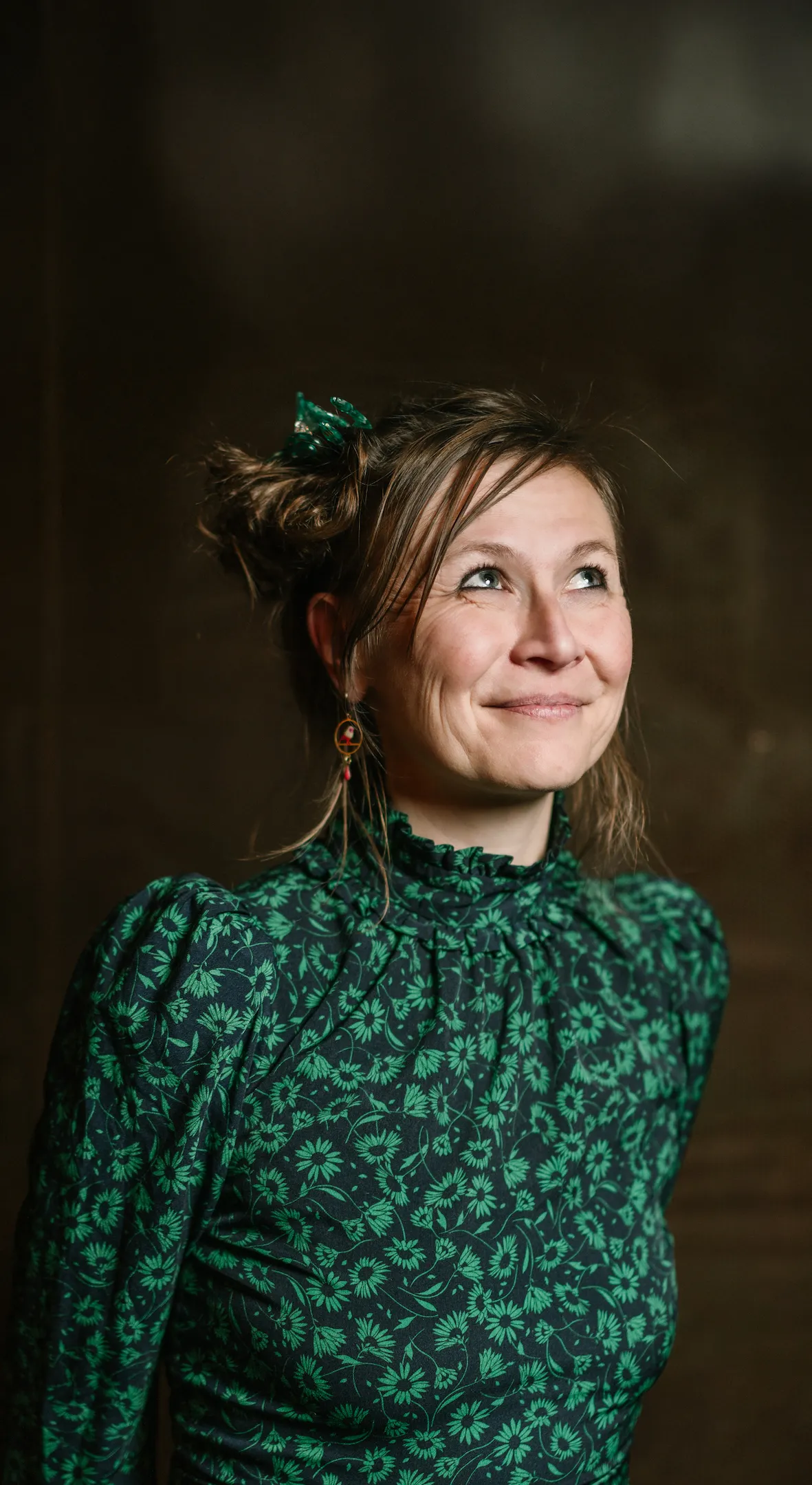 Femme souriante vêtue d'une robe verte à motifs floraux, regardant vers le haut à droite.