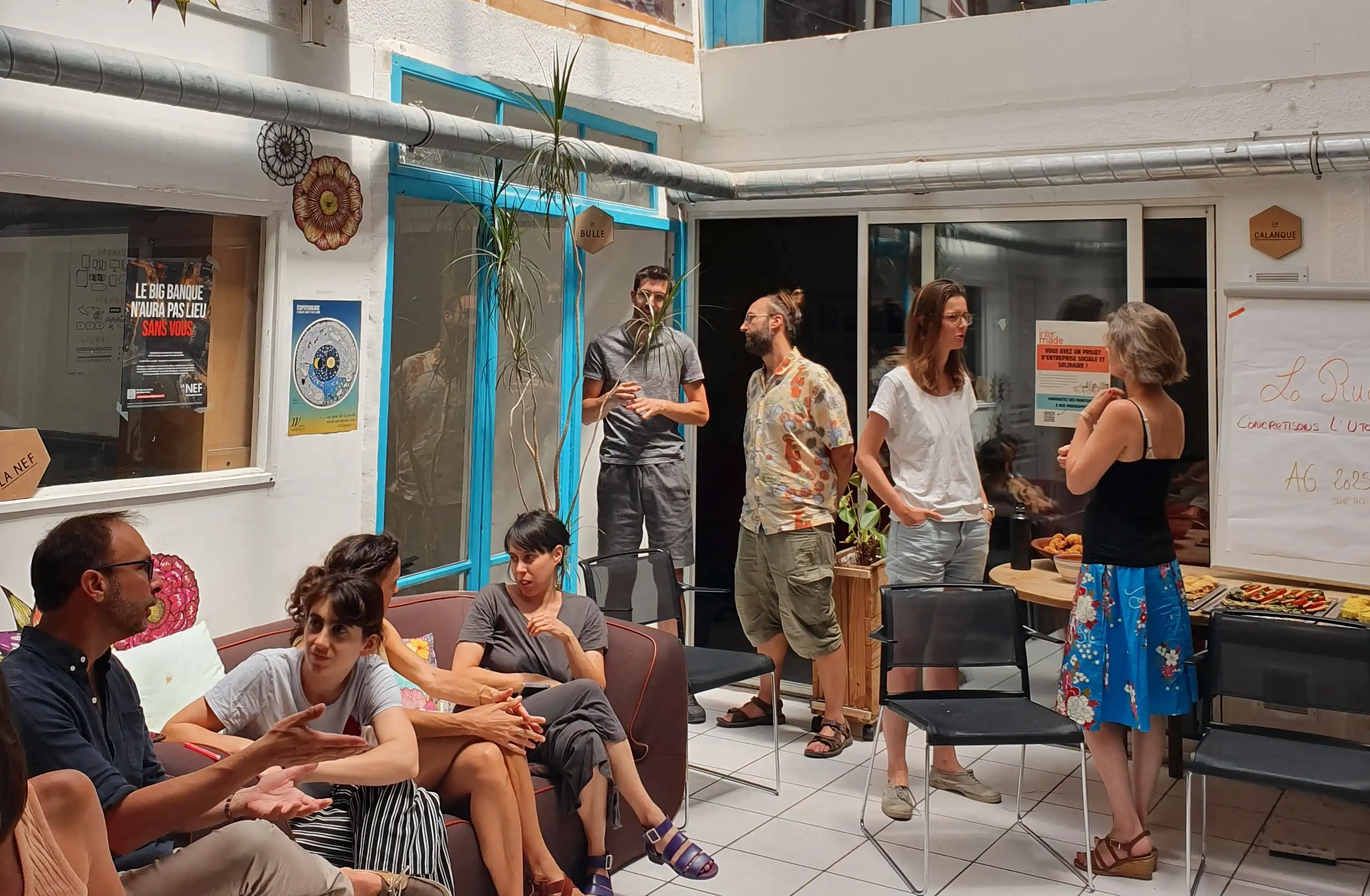 Un groupe de personnes discutant dans une salle lumineuse avec des chaises et un buffet de collations.