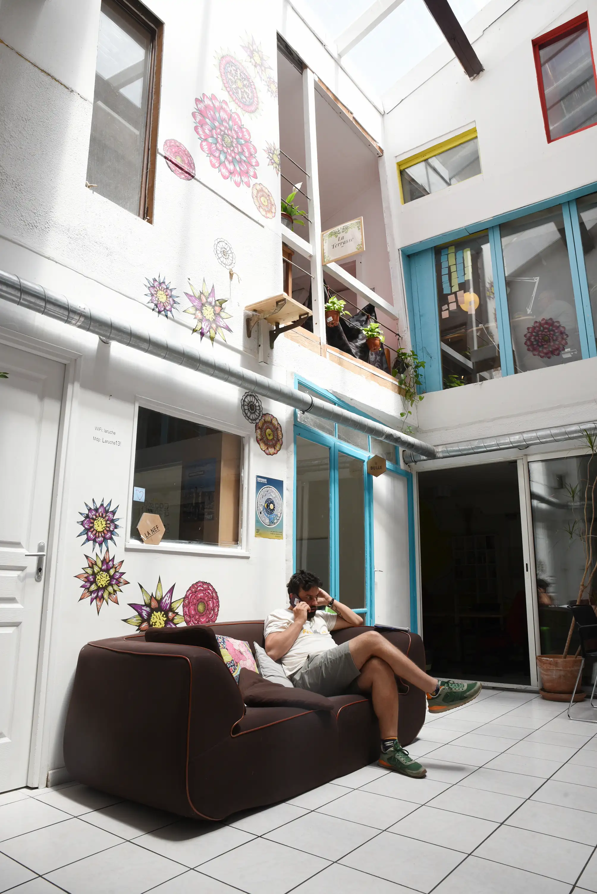 Un homme assis sur un canapé brun dans un espace de coworking lumineux avec des décorations murales florales.