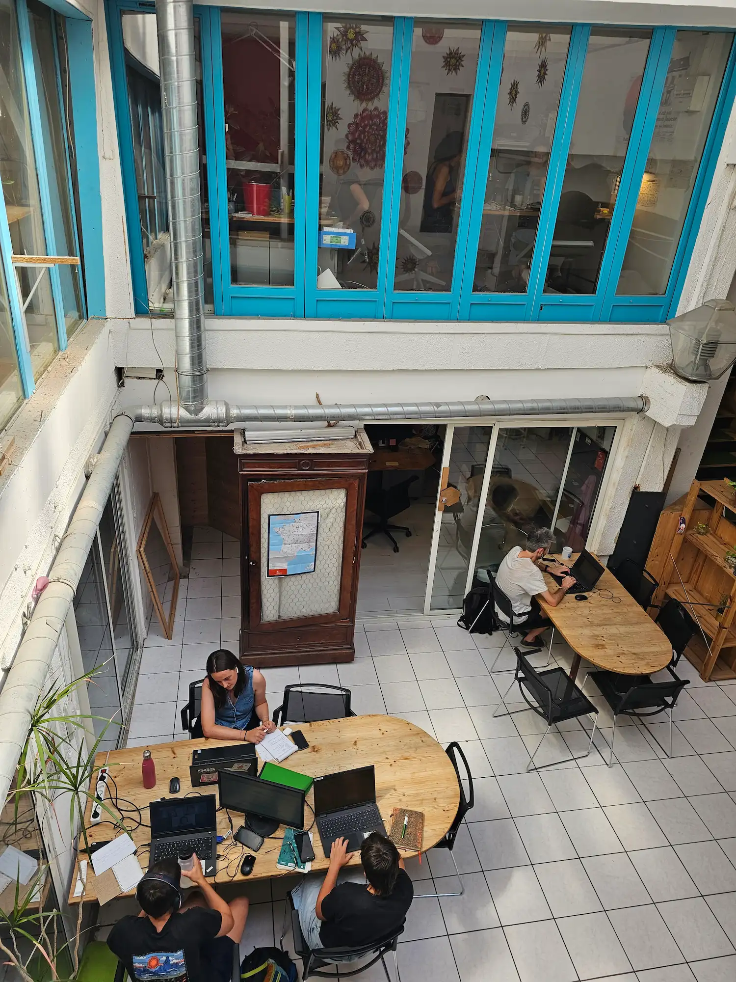 Quatre personnes travaillent sur ordinateurs portables à deux tables en bois dans un espace de coworking lumineux.