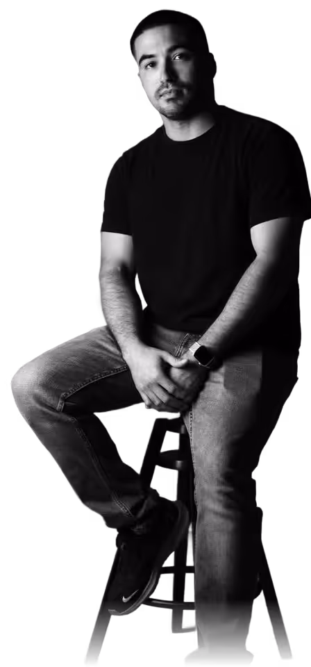 Manuel Mojica wearing black t-shirt and jeans sitting on a stool.