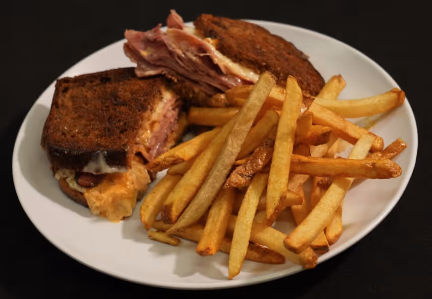 Plate with grilled sandwich and a serving of golden French fries on a black background.