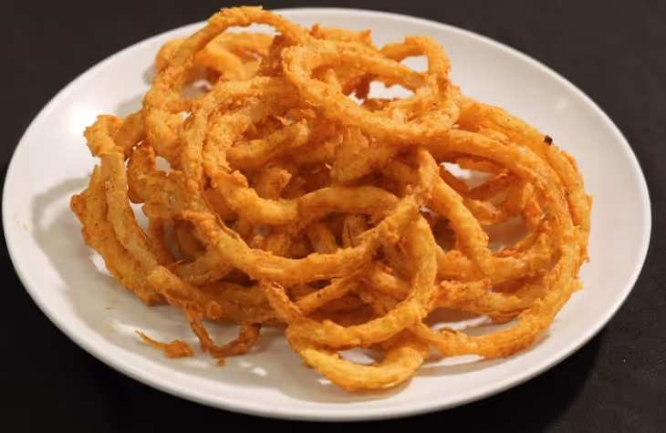 White plate piled with golden brown crispy fried onion rings on a black surface.