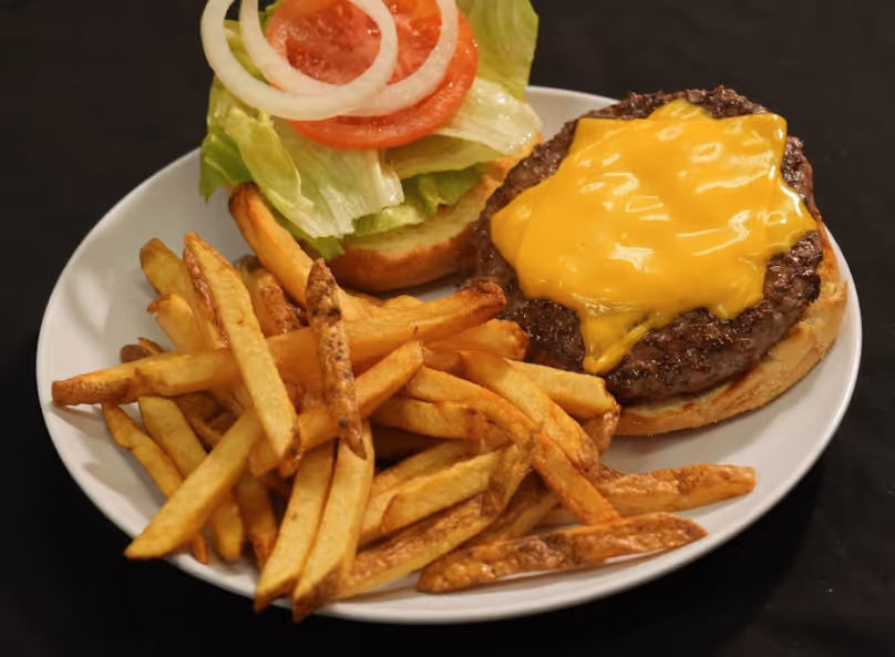 Cheeseburger with lettuce, tomato, and onion served with a side of French fries on a white plate.