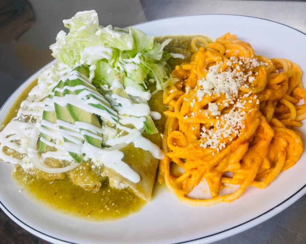 Plate with enchiladas topped with avocado slices, lettuce, and cream, served with creamy orange pasta sprinkled with cheese.