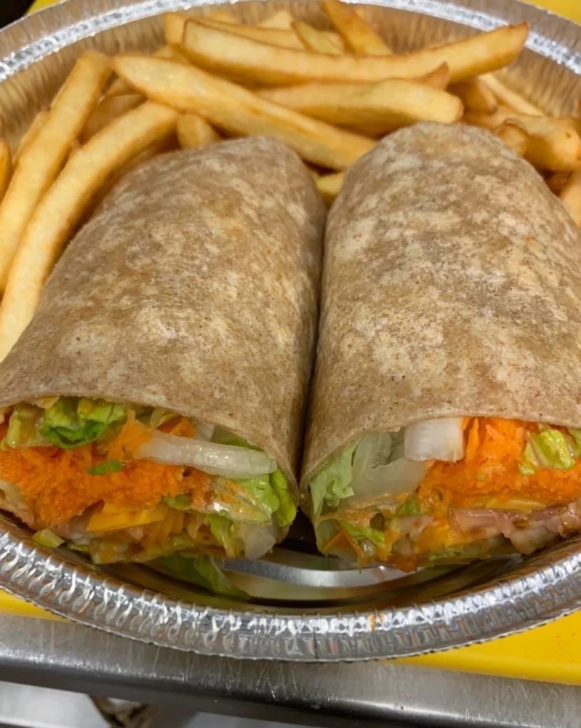 Two wraps filled with lettuce, shredded carrot, onion, and cheese served with French fries in a foil container.