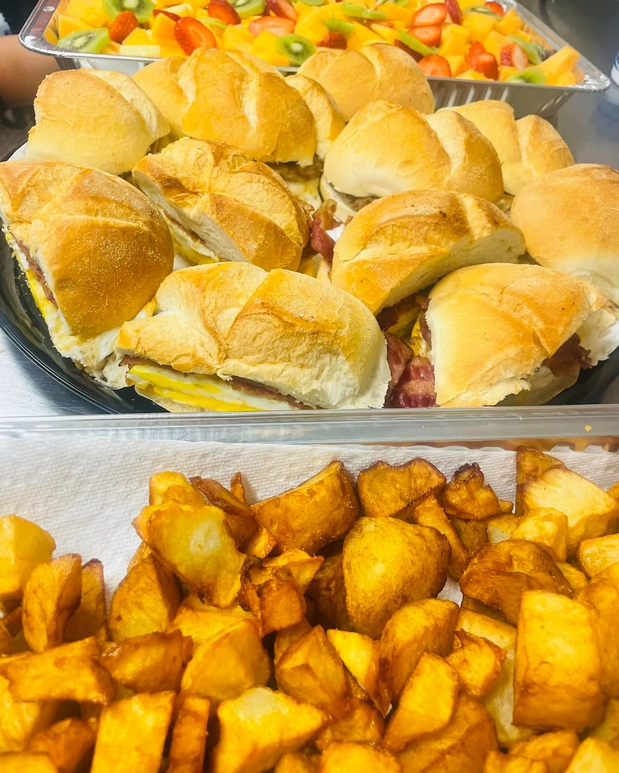 Tray with breakfast sandwiches, fried potato chunks, and a fruit salad with kiwi and strawberries.