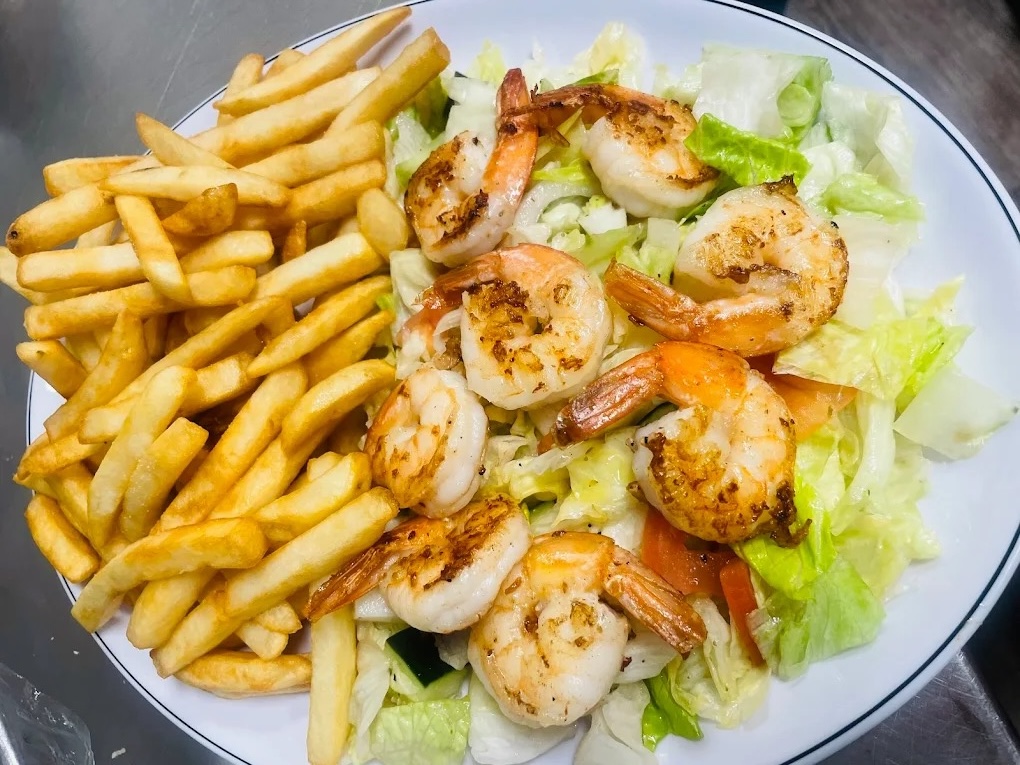 Plate with grilled shrimp on a bed of lettuce, tomato, and cucumber, served with French fries.