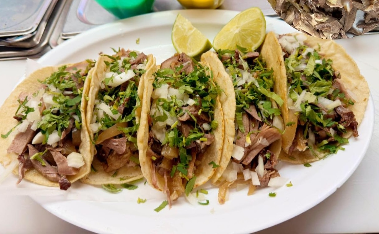 Five tacos filled with chopped meat, onions, and cilantro on a white plate with lime wedges.
