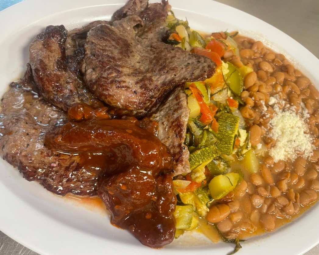 Plate with grilled steak topped with sauce, cooked mixed vegetables, and pinto beans with cheese.