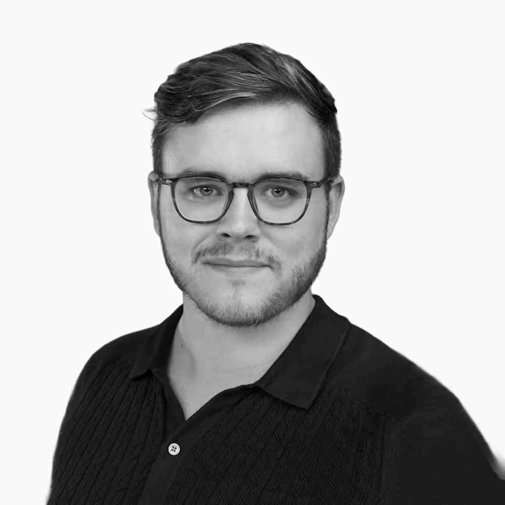 Professional black and white headshot of David, Partner and VP of Operations at Key Outreach, wearing glasses and a black textured polo shirt while posing against a light gray background.
