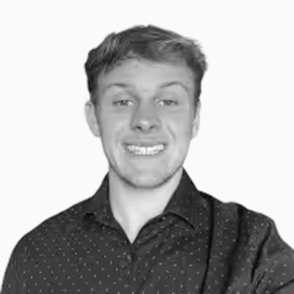 Professional black and white headshot of Ean, Client Success Representative at Key Outreach, smiling while wearing a dark patterned button-up shirt against a light gray background.