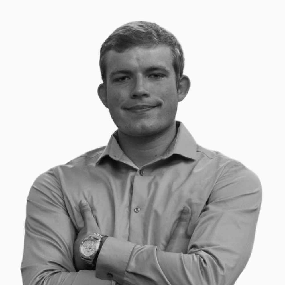 Professional black and white headshot of Keegan, Business Development Representative at Key Outreach, posing with arms crossed while wearing a light dress shirt and wristwatch against a light gray background.