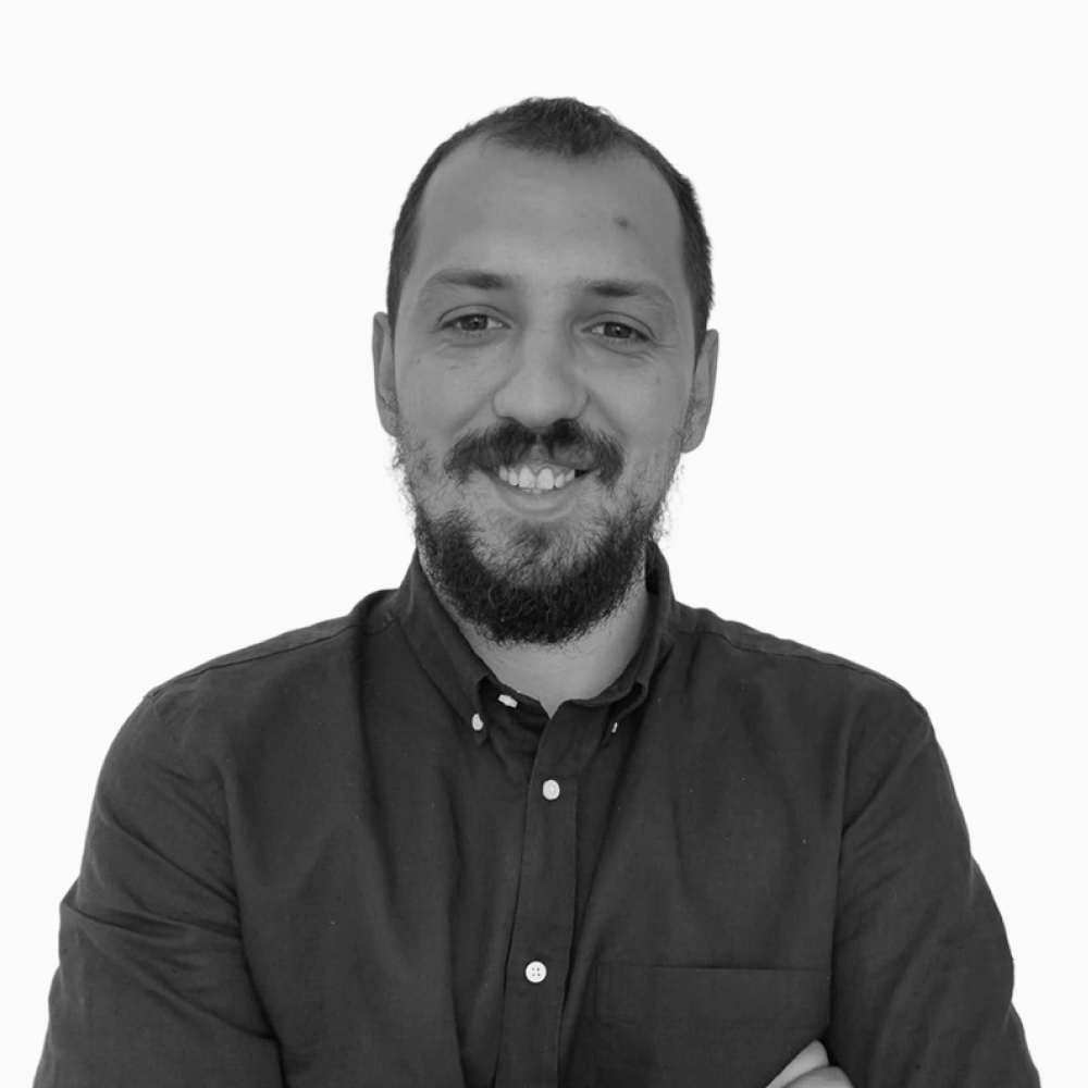 Professional black and white headshot of Milan, Client Success Representative at Key Outreach, smiling while wearing a dark button-up shirt with arms crossed against a light gray background.