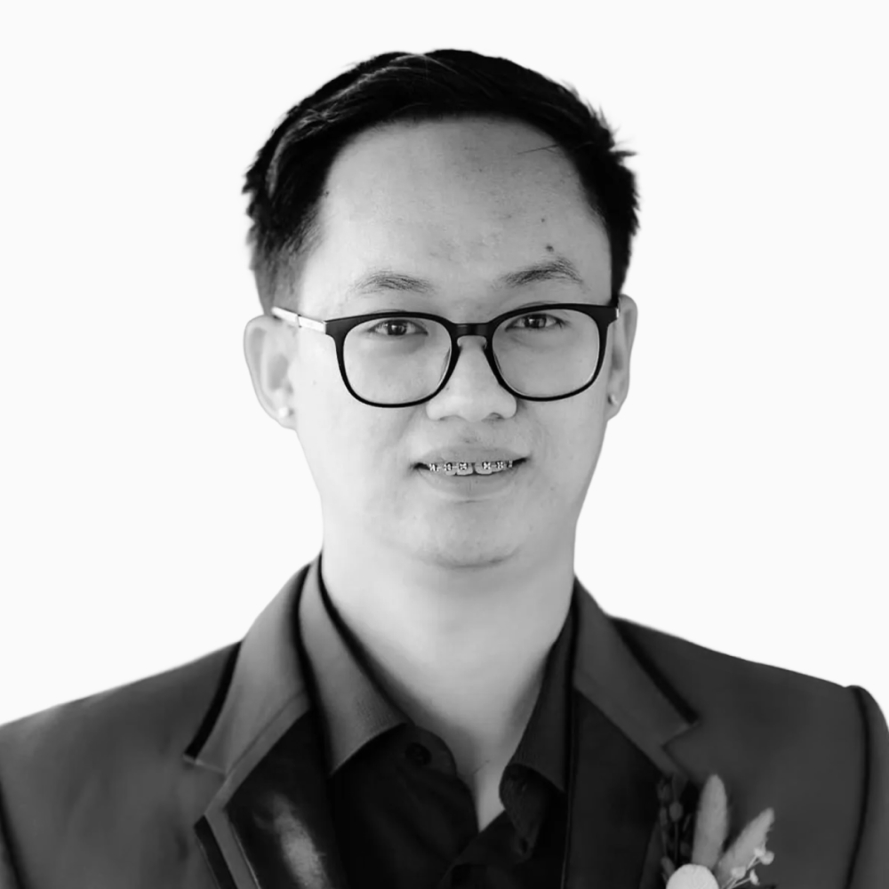 Professional black and white headshot of Sky, SOR Team Lead at Key Outreach, wearing glasses, braces, and a suit jacket over a dark dress shirt while posing against a light gray background.