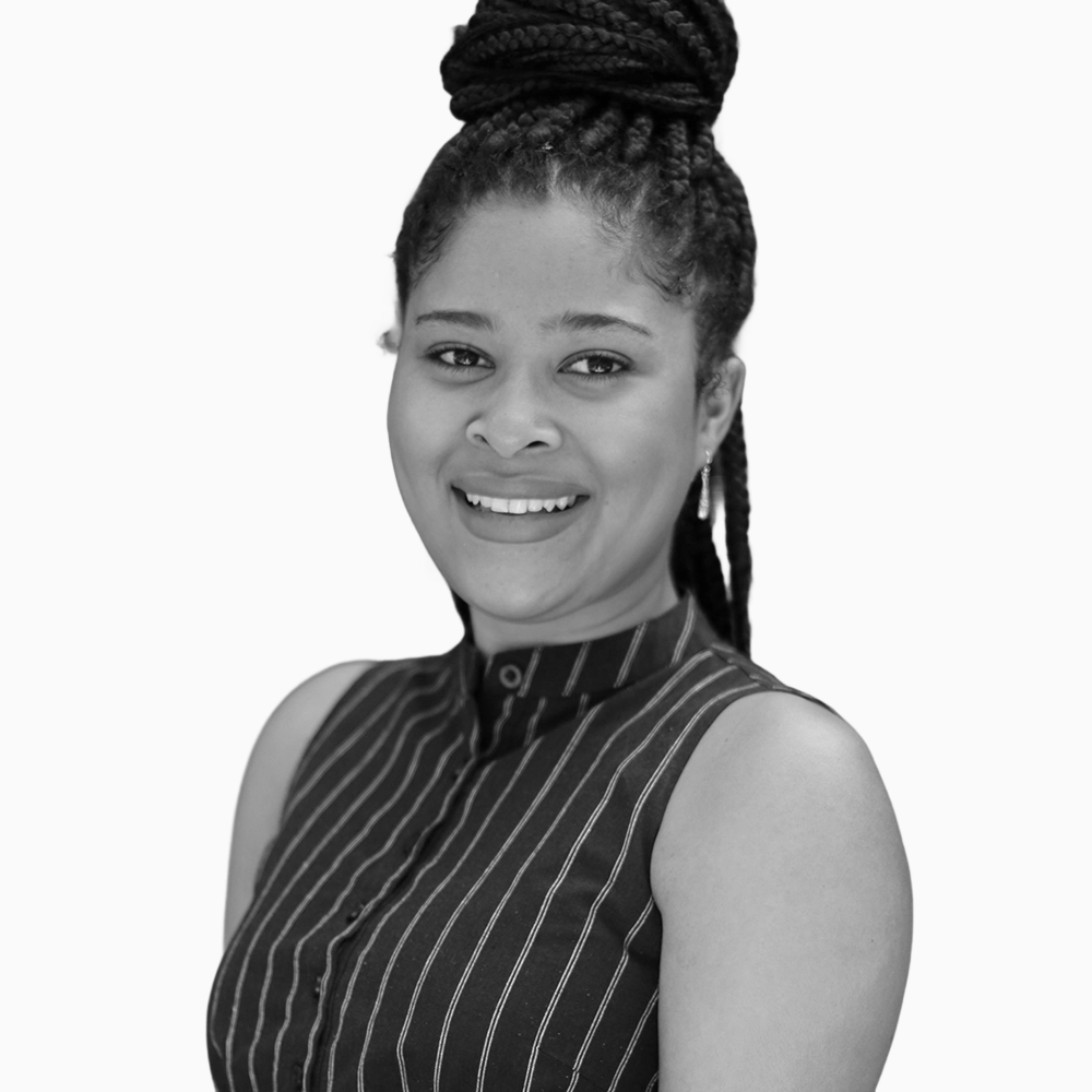 Professional black and white headshot of Tatum, Copywriter at Key Outreach, smiling while wearing a sleeveless striped blouse and braided updo hairstyle against a light gray background.