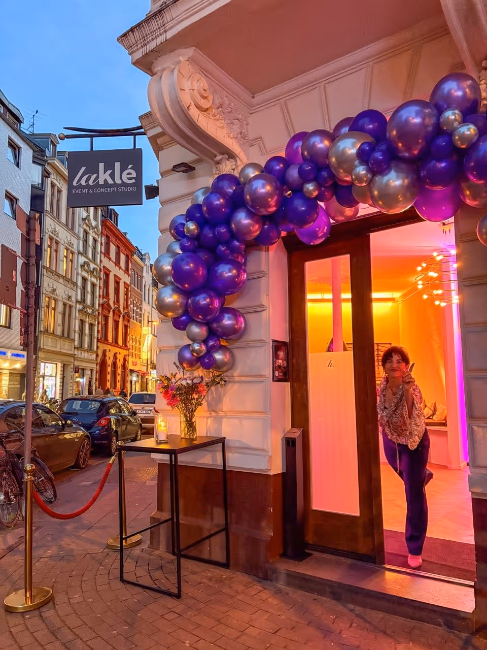 Entrance of laklé event studio decorated with purple and silver balloons and a woman making a peace sign.