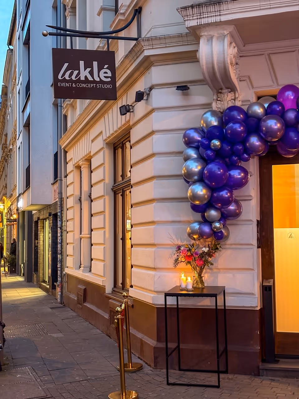 Street view of laklé event studio entrance decorated with purple and silver balloons and a flower vase with candles.