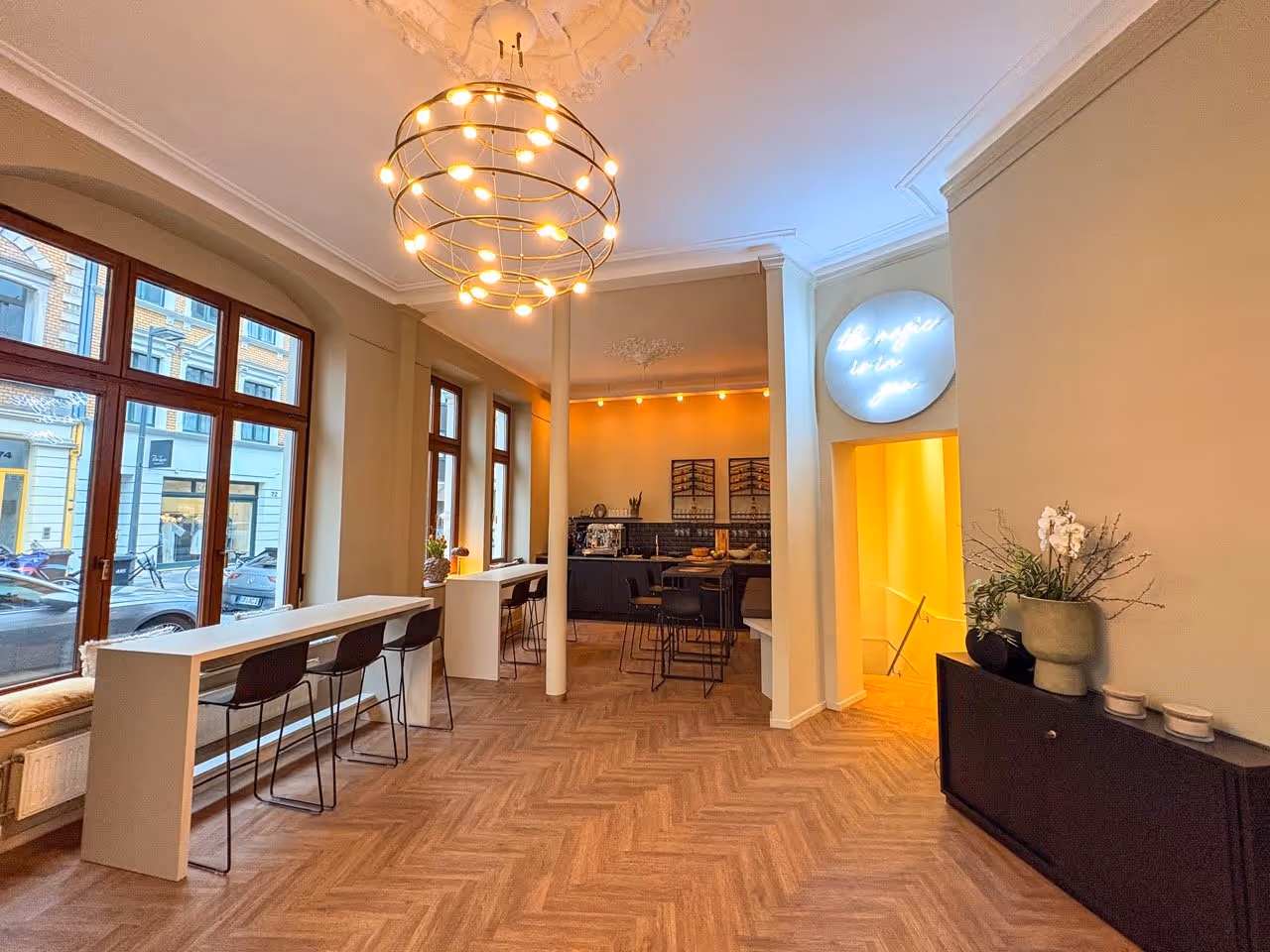 Modern room with large windows, pendant light, bar seating, and a kitchen area with black chairs.