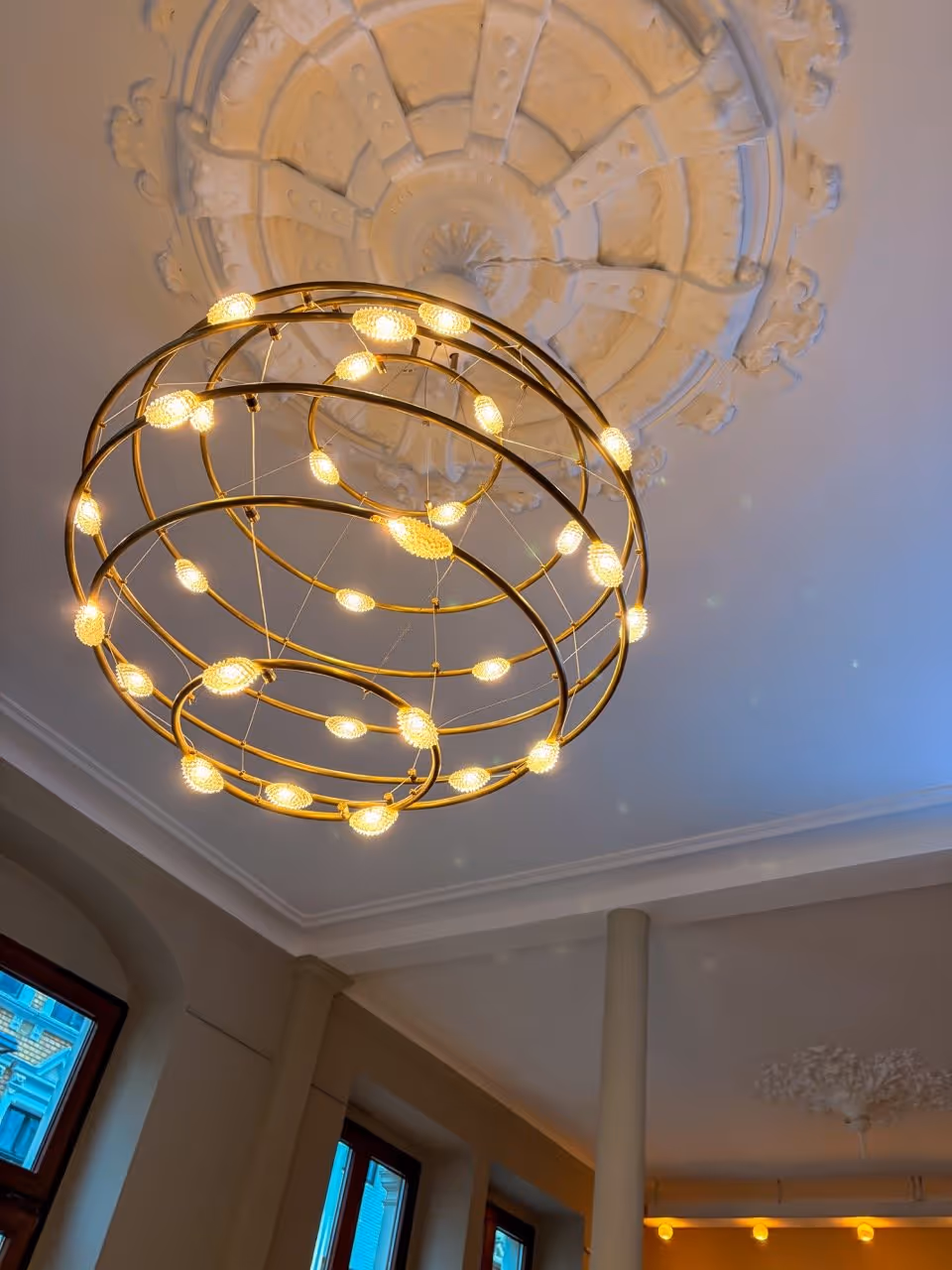 Modern circular chandelier with warm lights hangs from a decorative ceiling medallion.