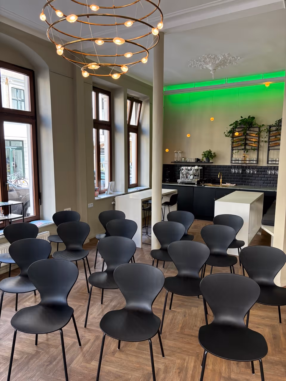 Modern room with black chairs in rows, large windows, and a bar area with green lighting.