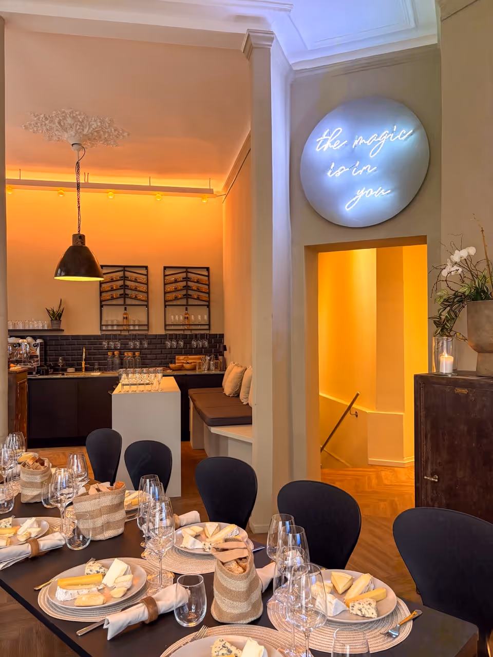 Elegant dining room set with cheese plates, wine glasses, and a neon sign saying 'the magic is in you'.
