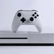 White gaming console with white wireless controller resting on top against white background.