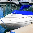 White motorboat with blue cover docked at a marina with other boats in the background.