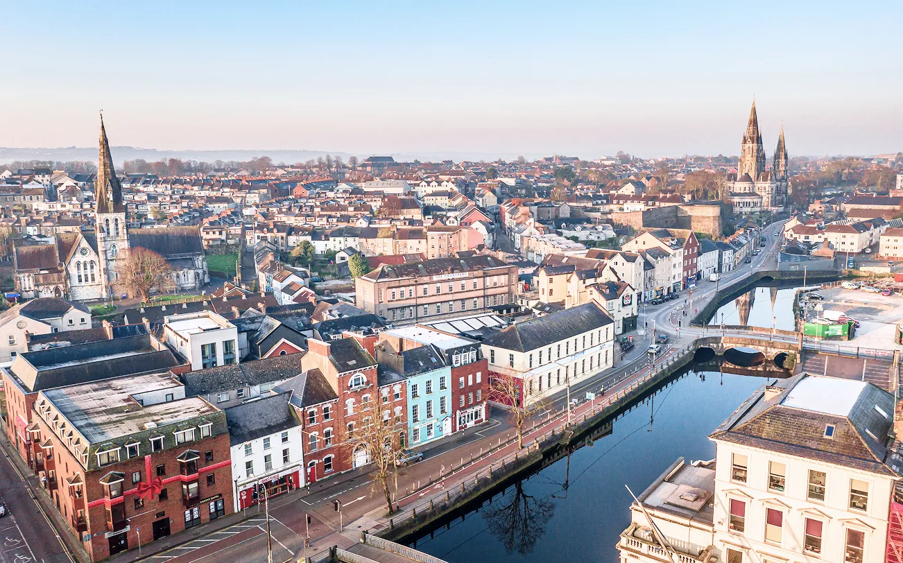 Aerial view of a city with a river, bridges, churches, and rows of houses under clear sky.