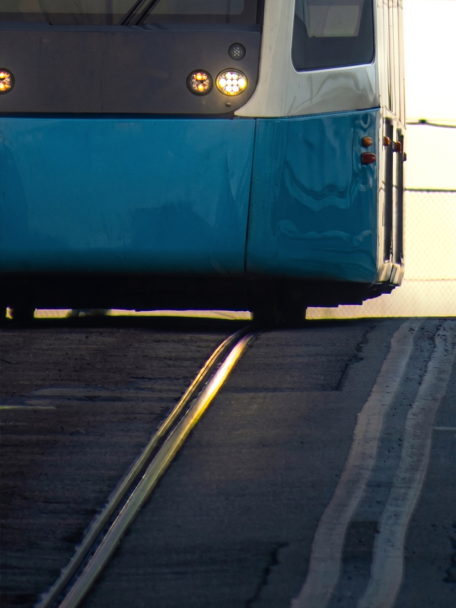A blue tram glides forward in the evening sun.