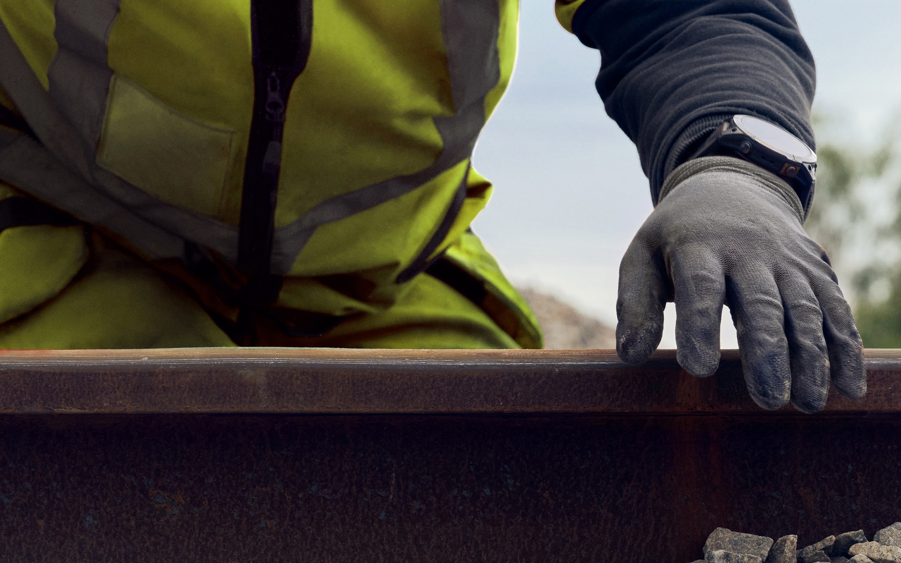 Track technician wearing protective glove and reflective vest inspects rails at close range.