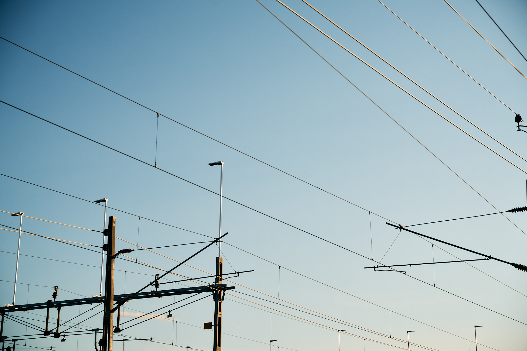 Network of power lines and poles against a clear blue sky.