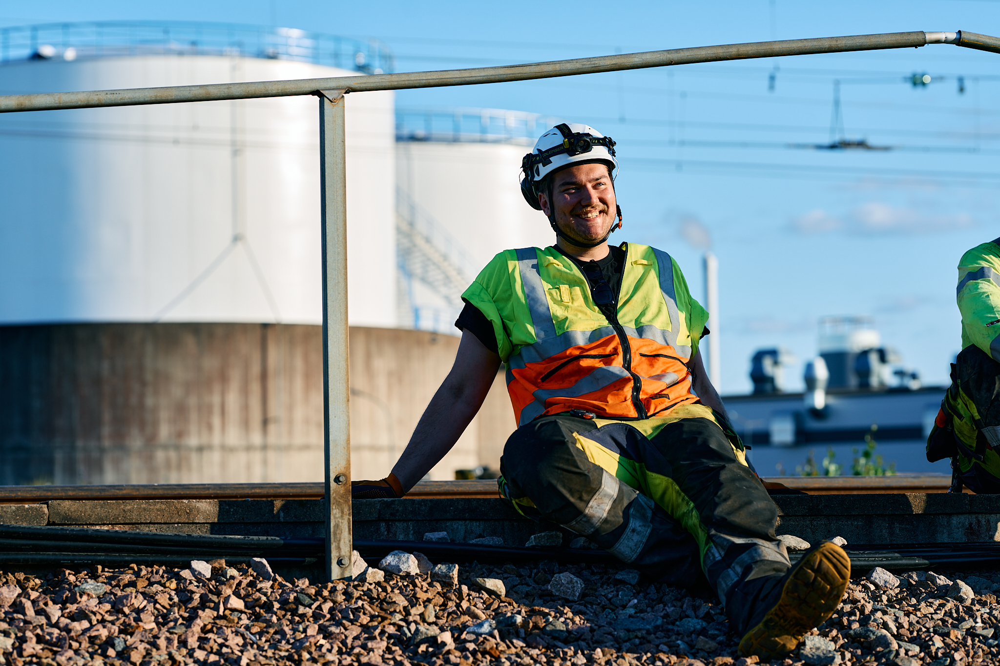 Track technician in protective helmet and reflective vest sitting and enjoying the sunshine at a work area.