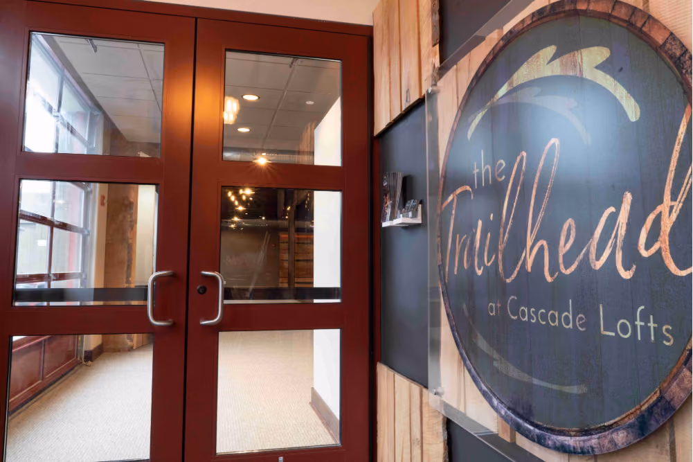 Entry with double glass doors next to a round sign reading 'the Trailhead at Cascade Lofts'.