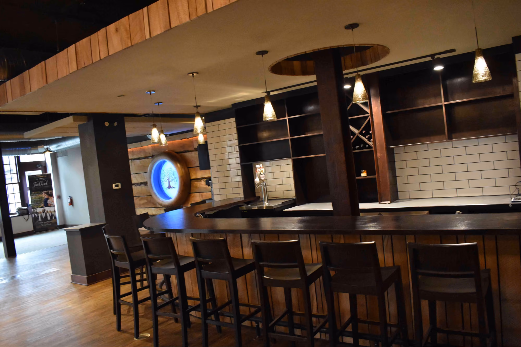 Empty curved wooden bar with bar stools and pendant lights in a modern interior with wood floors.