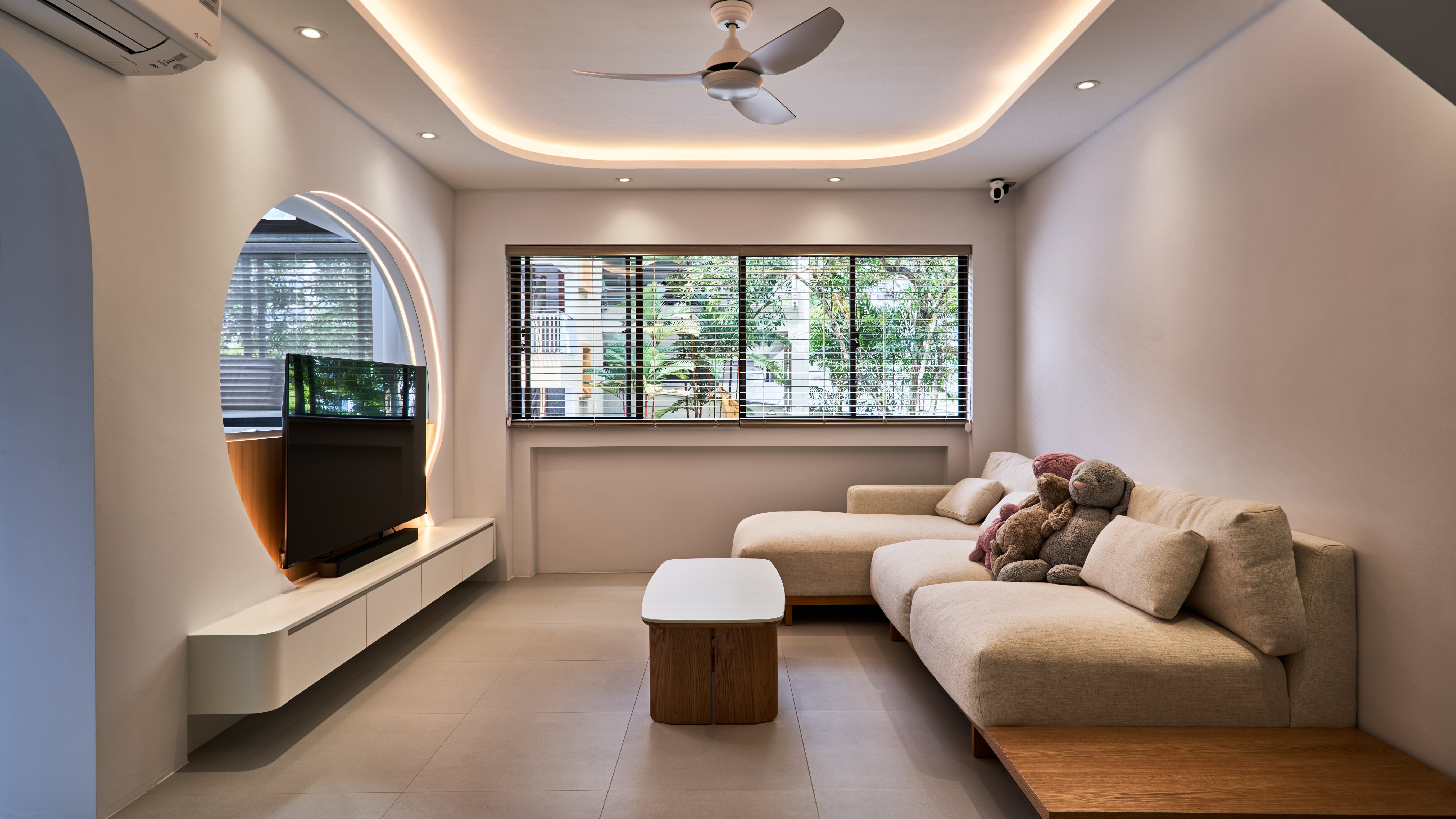 Warm minimalist living room with curved TV feature wall, arched mirror, sectional sofa and soft ambient lighting.