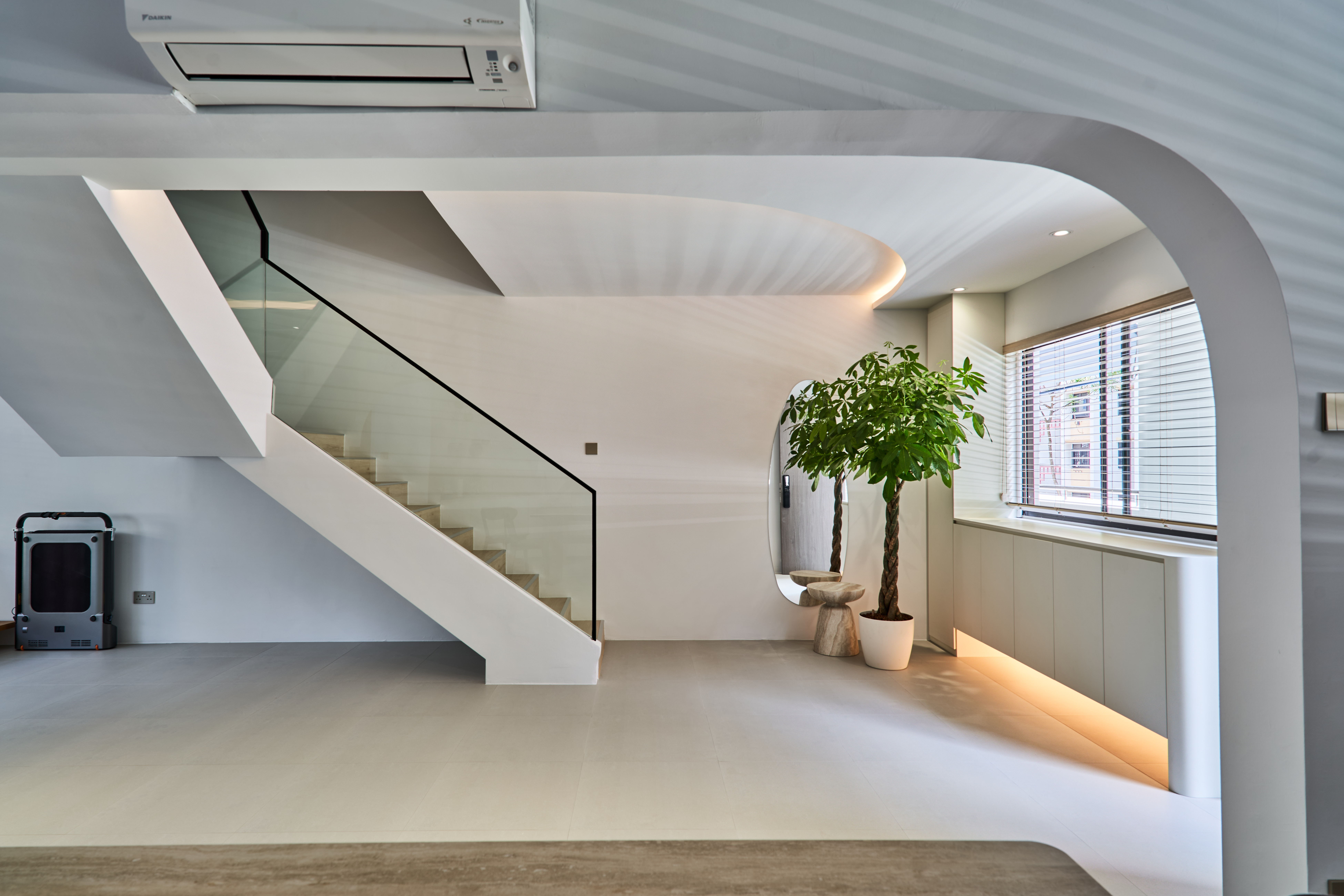 Modern staircase with glass railing beneath a sculptural arched ceiling, with a potted plant and built-in window seating in the background.
