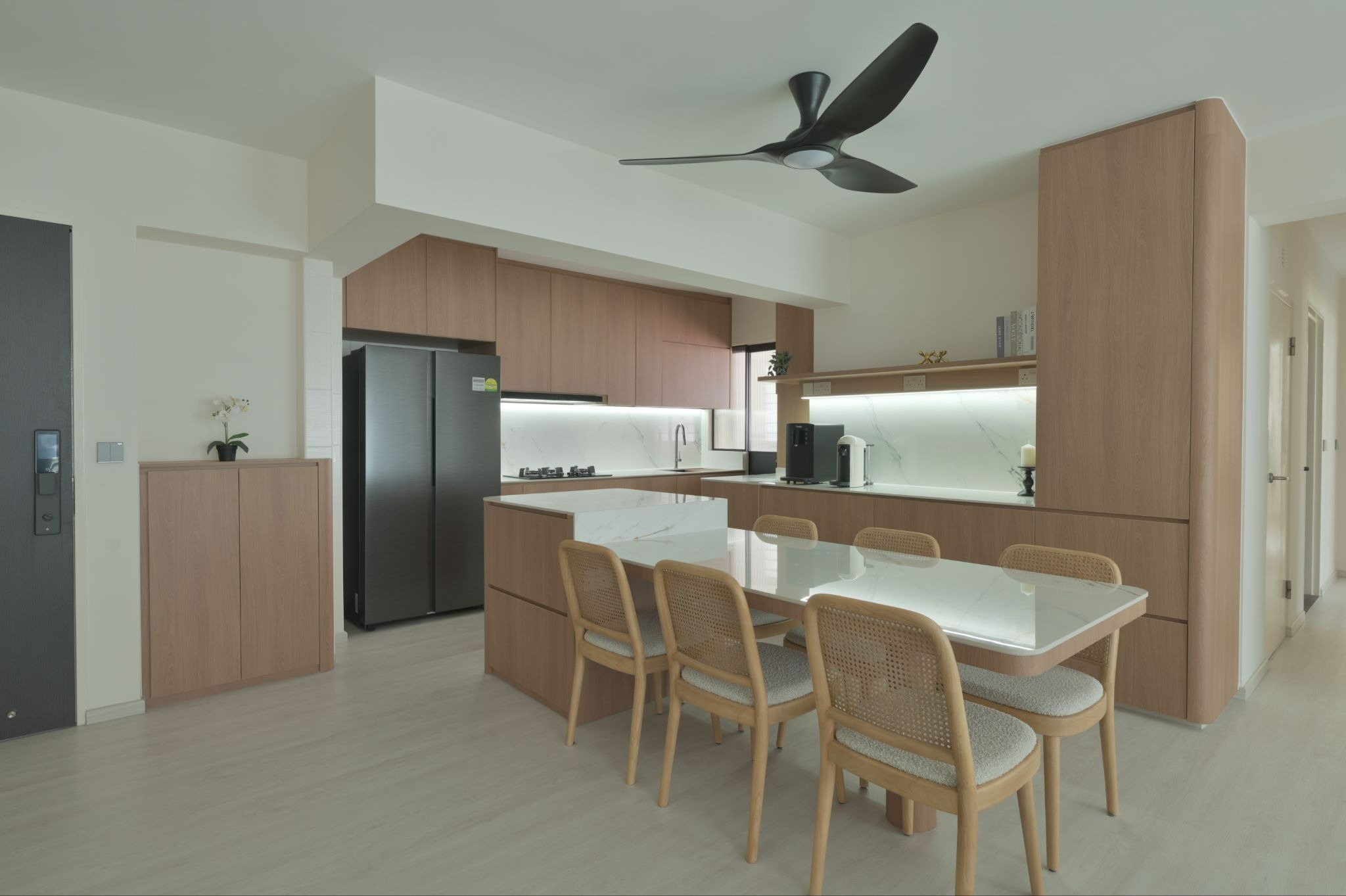 Modern HDB kitchen with warm wood cabinets, a white marble-look dining island, built-in storage and under-cabinet lighting in Singapore.