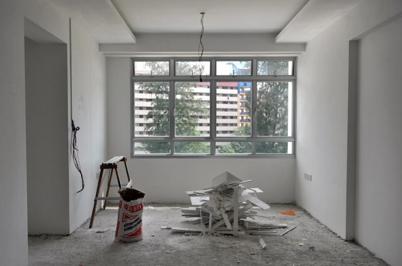 Unfinished HDB living room with bare flooring, construction debris, exposed wiring and a large window during renovation.