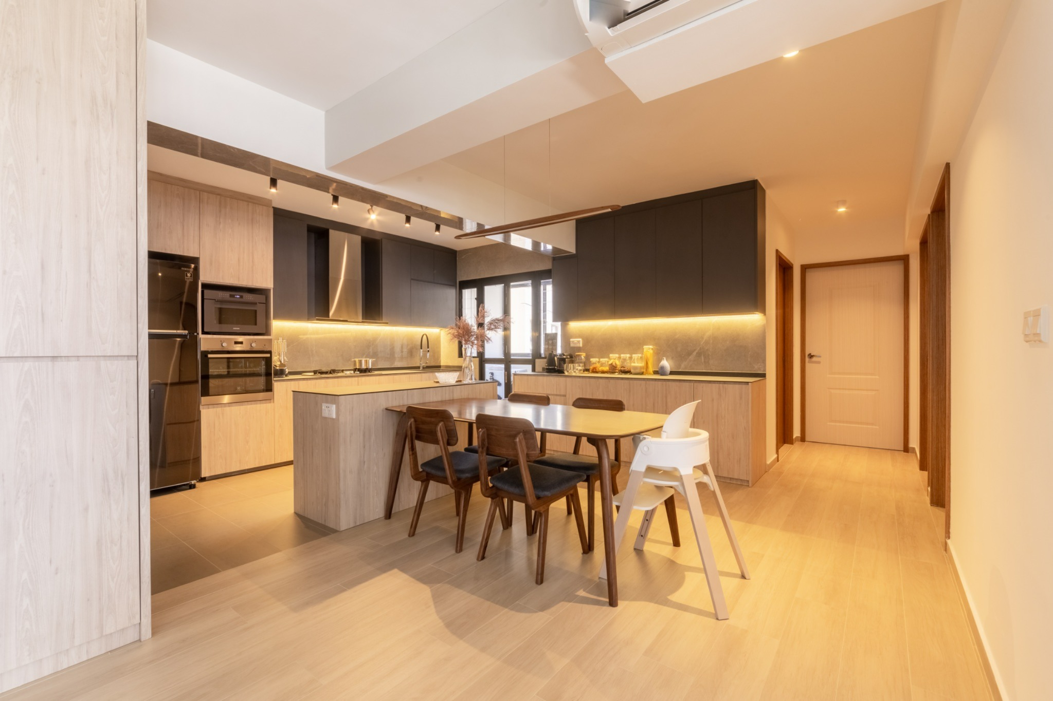 Open-plan kitchen with light wood cabinets, dark upper cupboards, under-cabinet lighting and a dining table.