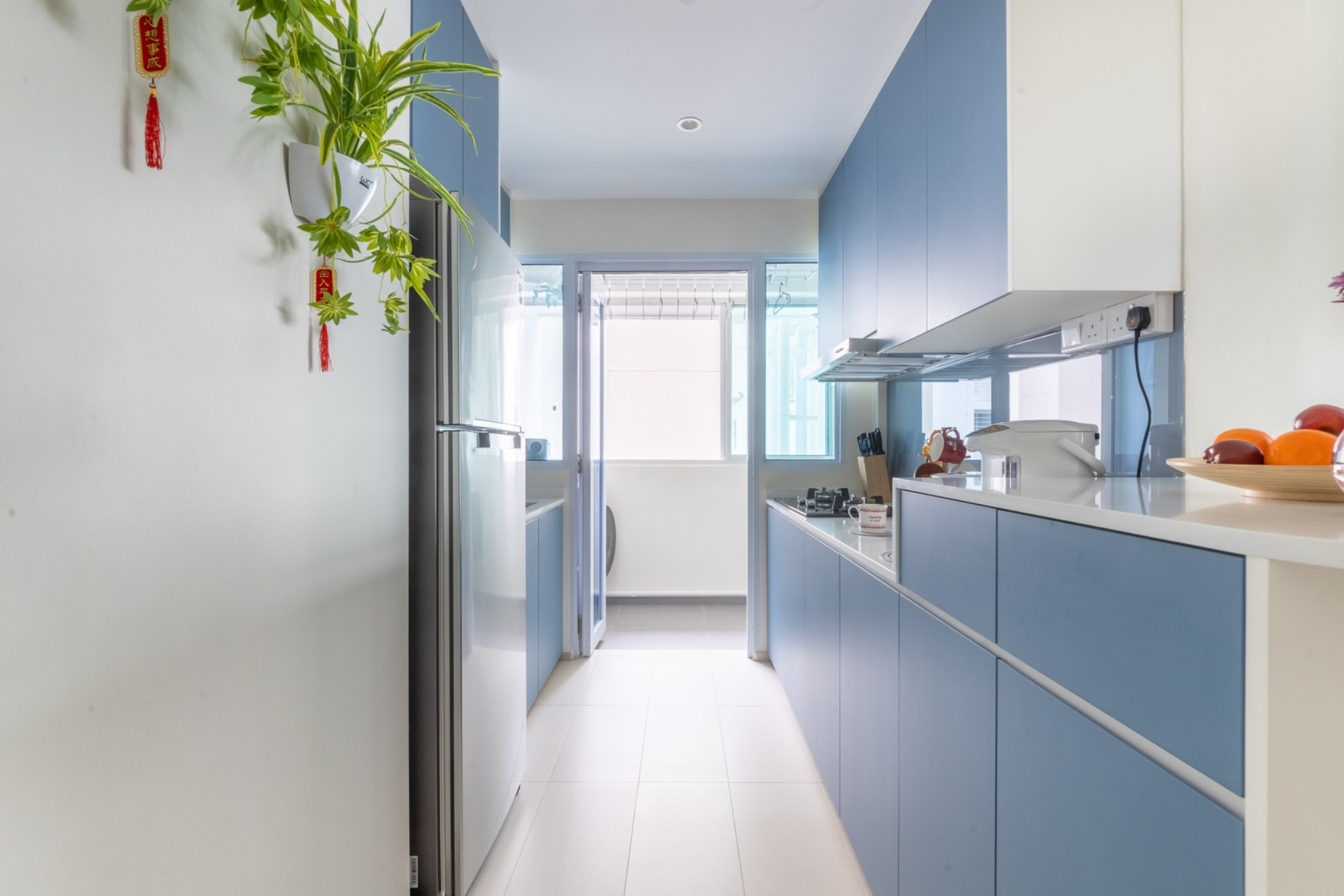 Narrow kitchen with blue cabinetry, white countertops and tiled flooring.