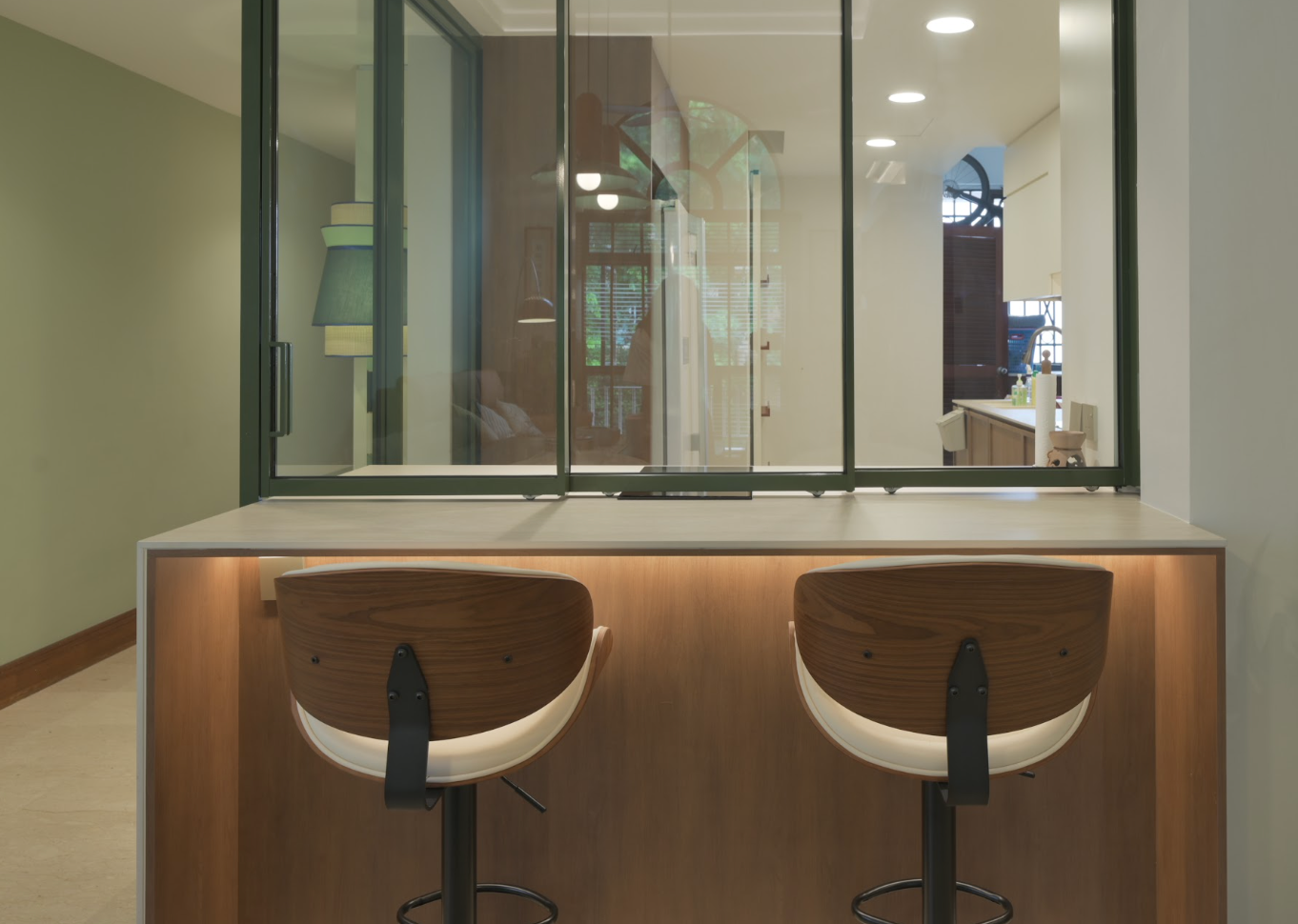 Custom wood-finish island with two bar stools beside black-framed glass partitions in a modern HDB home.