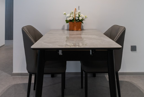 Minimal dining area with a rectangular stone-look dining table, two dark upholstered chairs and a flower arrangement in a modern HDB home.