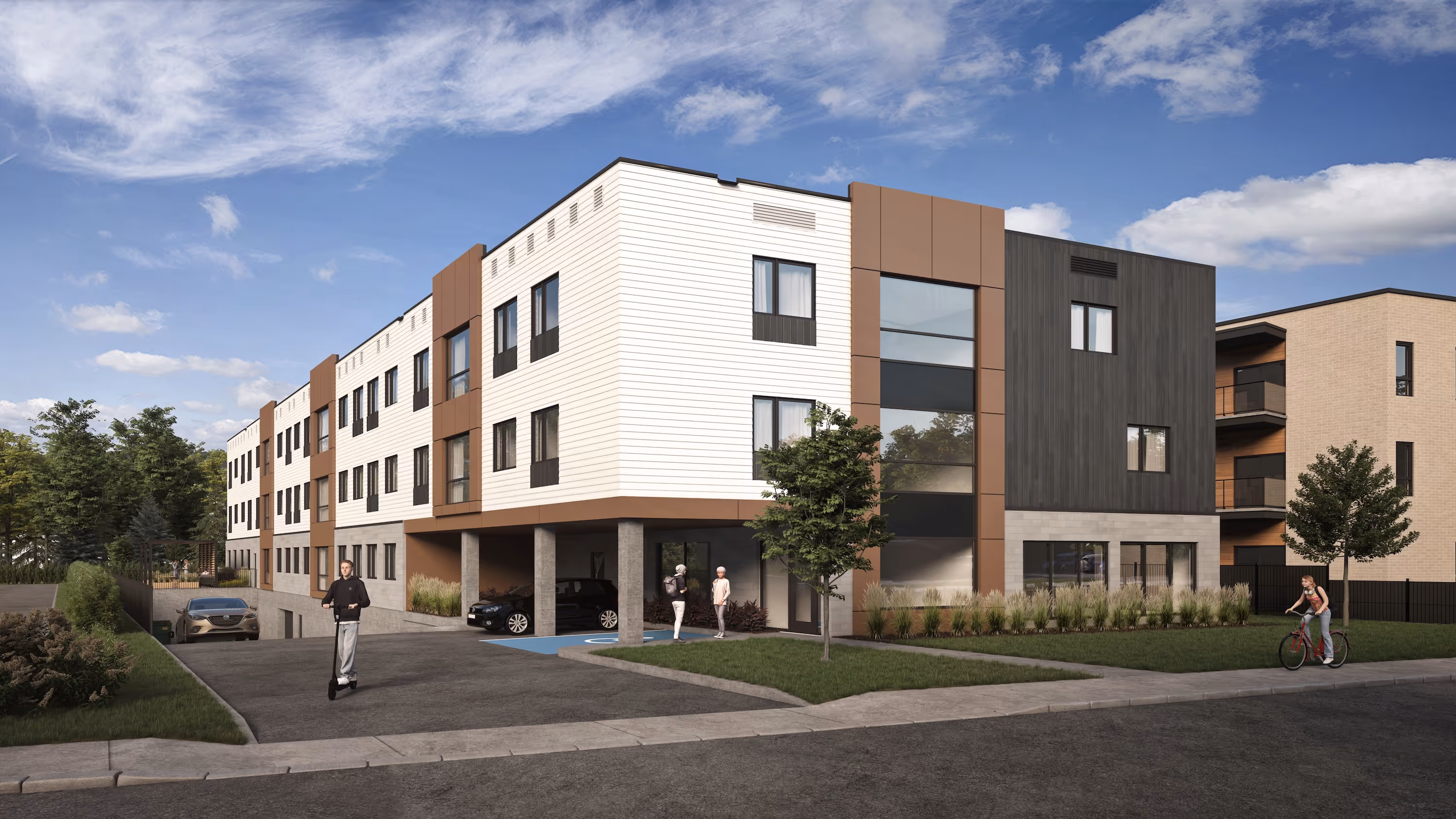 Modern three-story apartment building with white, brown, and dark gray exterior panels, featuring large windows and a covered parking area beneath, set against a partly cloudy sky with trees and shrubs around the property and people walking and biking nearby.
