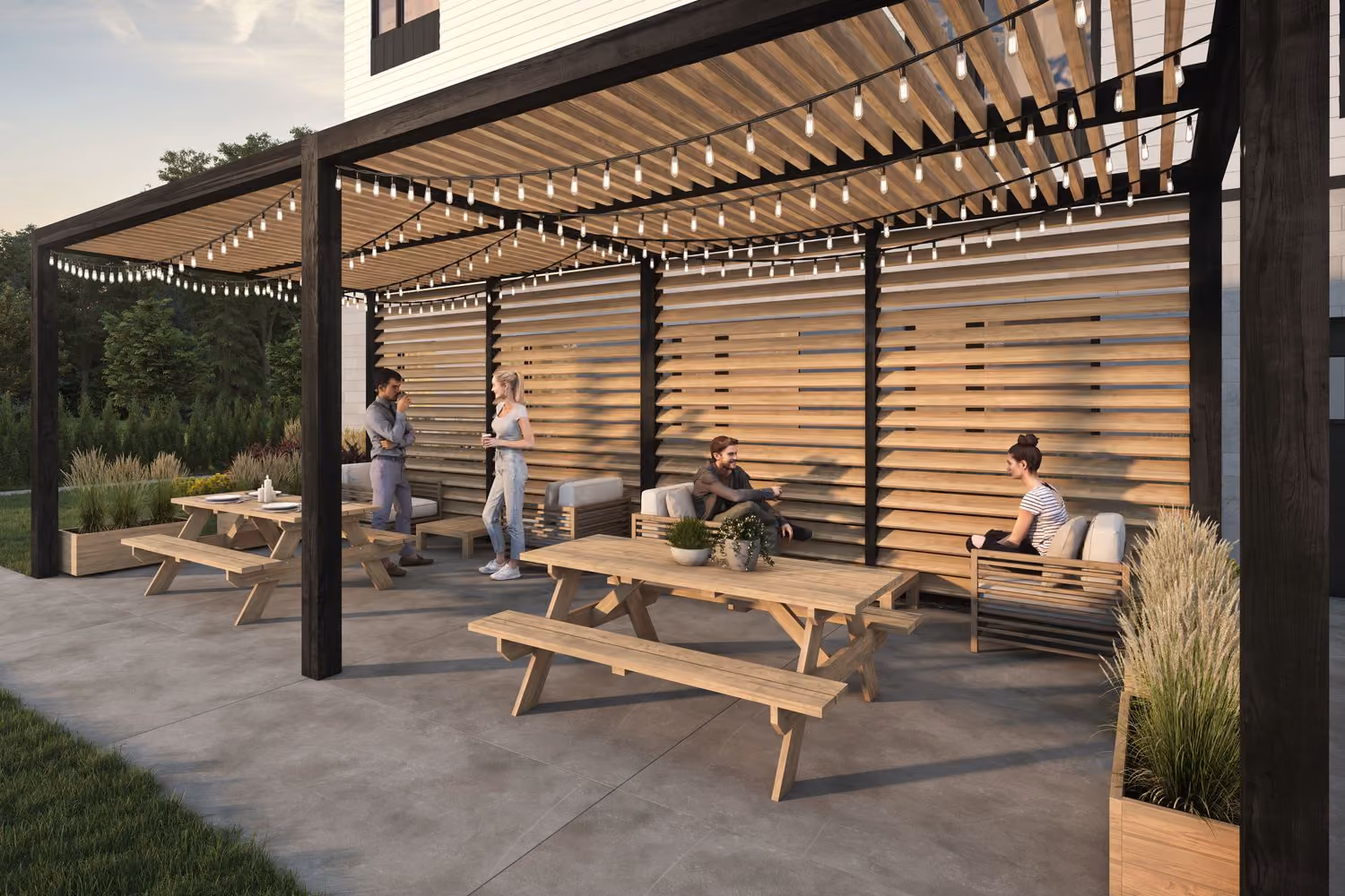 Modern outdoor patio area with wooden picnic tables and cushioned benches under a pergola with string lights, featuring two people standing and talking on the left and two people sitting and conversing on the right, surrounded by planters with greenery and grasses.