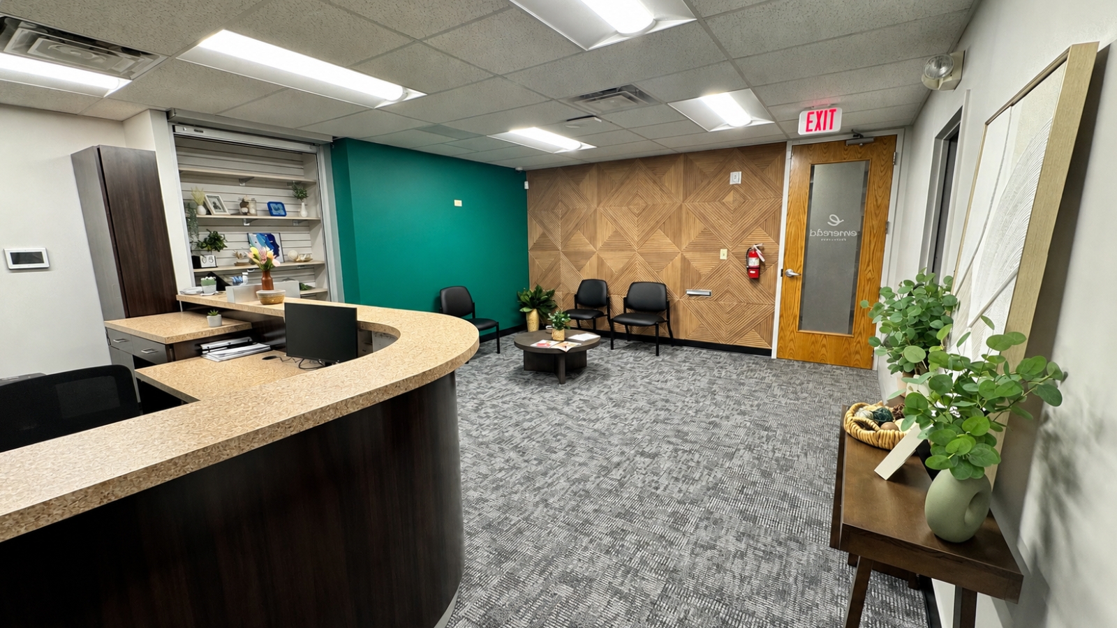 Modern office lobby with curved reception desk, waiting chairs, green accent wall, and decorative plants.