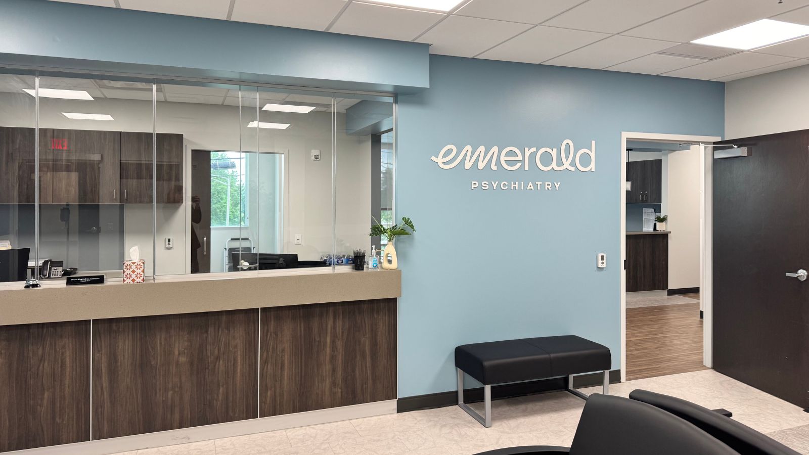 Reception area of Emerald Psychiatry with blue wall, reception desk, and black bench seating.