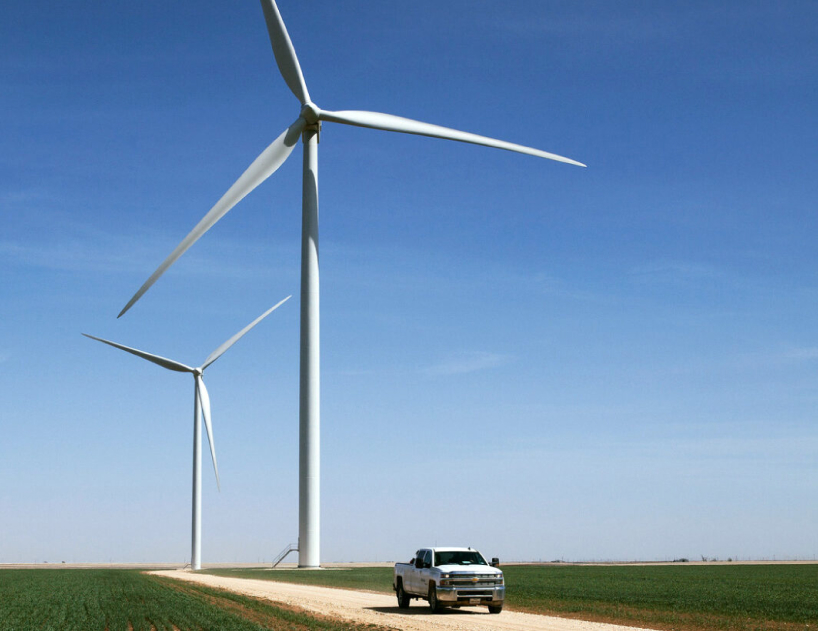 truck driving down a dirt road with wind turbines in the background