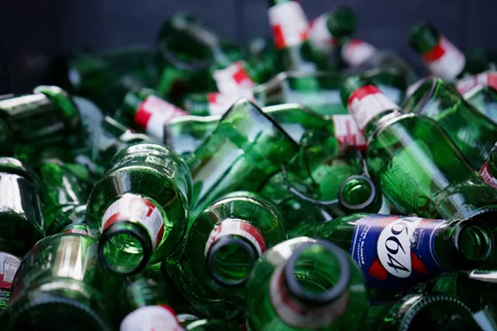 Pile of empty green glass bottles with white and red labels, some with a blue label showing the number 1964.